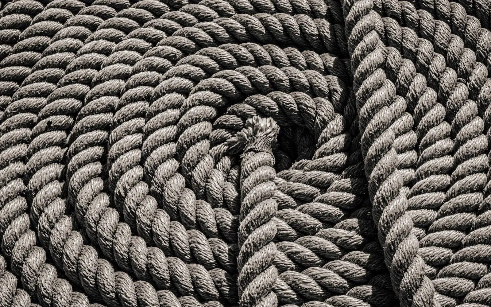Zu einer Spirale aufgerolltes, gedrehtes Naturfaserseil in Grautönen – Sinnbild für Shibari, die japanische Seilkunst