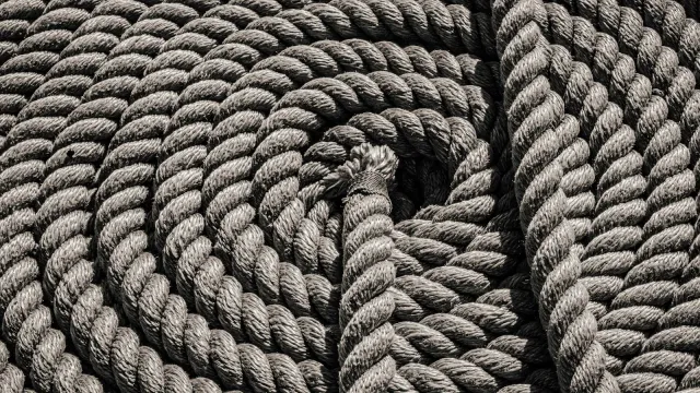 Zu einer Spirale aufgerolltes, gedrehtes Naturfaserseil in Grautönen – Sinnbild für Shibari, die japanische Seilkunst